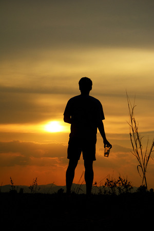 silhouette of a lonely man holding a beer glass looking at the sunsetの写真素材