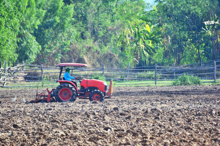 Farmer in tractor plowing land with red tractor for agricultureの写真素材