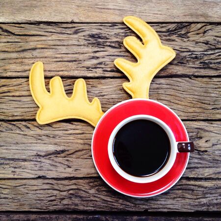 Coffee cup with reindeer headband on wooden board background.の素材