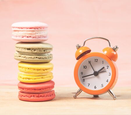 Macaroons and alarm clock on table, vintage stylized photo