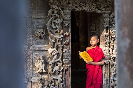 MANDALAY,MYANMAR-FEB 18 : Young monks standing and reading at Shwenandaw Monastery is built in the traditional Burmese architectural style on February 18,2015 in Mandalay,Myanmar.のeditorial素材