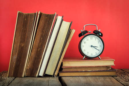 Vintage still life of stack of old books with alarm clock on red or pink background.の写真素材