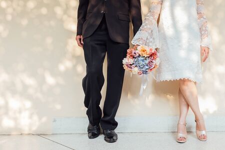Legs pretty young loving couple on the wall with bouquet and soft sunlight. Love, wedding concept.の写真素材