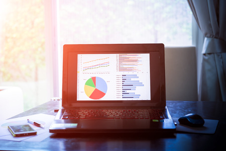 Laptop on wooden table showing charts and graph against office background ,Analysis Business Accounting, Statistic Concept. Vintage color filtered.の写真素材