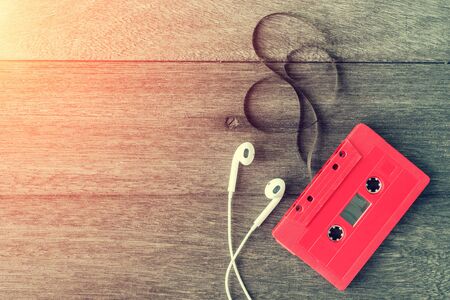 Red cassette tape with earphone over wooden table. top view. Retro or vintage color filtered. Old...