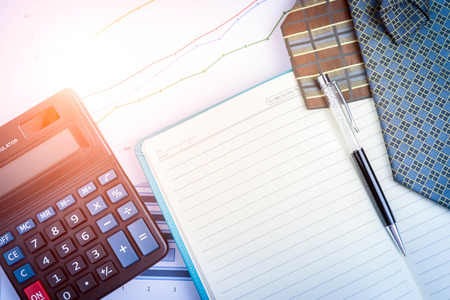 Business analysis on a wooden Desk with notebook, charts, pen, calculator and neckties. Vintage color filtered.の写真素材