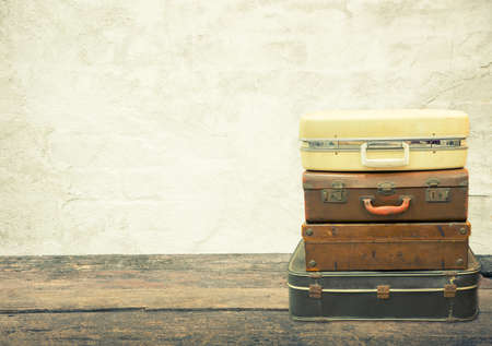 Stacked leather luggage on wood plank with old concrete background. Travel concept.の写真素材