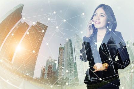 Businesswoman using a mobile phone and looking forward to city with network connection smart city. International business, world wide business connecting technology concept.の写真素材