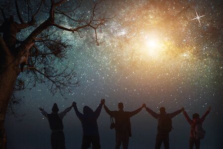 Milky Way.Night sky with stars and silhouette of standing happy peoples raised up arms.Blue milky way with people on the mountain.Background with universe.Night light landscape.Travel freedom concept.の写真素材
