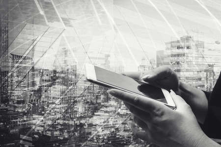Businessman holding smart phone with wireless communication network icon and cityscape...