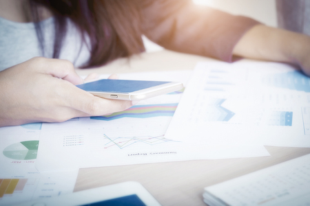 Businesswoman working in office and using smartphone with business diagrams on table. Finance office workplace.の写真素材