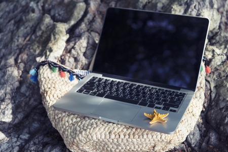 Business and technology with nature in vacation concept. Empty laptop screen put on summer traveling bag on the beach. Nomad or freelance. Picture for add text message. Backdrop for design art work.の写真素材