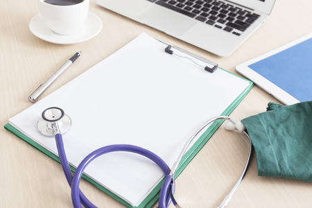 Blank medical clipboard and stethoscope on wooden desk, workplace of a doctor background.の写真素材