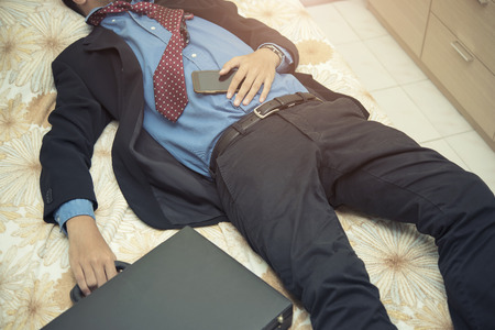 Tiredness businessman sleeping in suit with bag and mobile on hand after hard worked.の写真素材