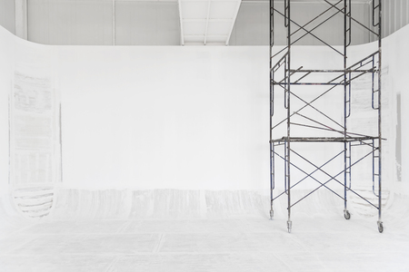 Construction and abstract background. White room renovating work process with white painted on wall and floor with scaffolding. Picture for add text message. Backdrop for design art work.の写真素材