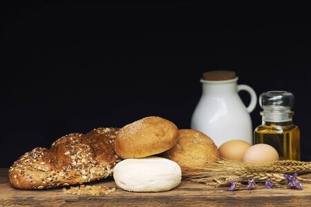 Breads, milk and oil on wood table with black background.の写真素材