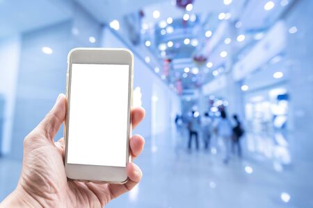 Technology background, hand holding mobile with empty screen and blurred shopping mall in background.の写真素材