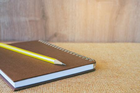 Brown note book and one pencils on brown background.