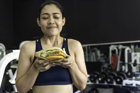 The girl is holding a hamburger happy after exercising in fitness, diet control with exercise as a principle of healthy care.の写真素材