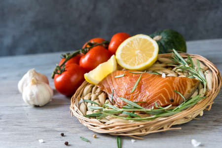 Grilled salmon steak on vintage wooden board with fork, olive oil, vegetables, herbs and spices on...