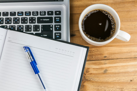 Laptop with coffee cup, notebook and pen on wooden background, concept for home officeの写真素材