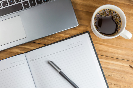 Laptop with coffee cup, notebook and pen on wooden background, concept for home officeの写真素材