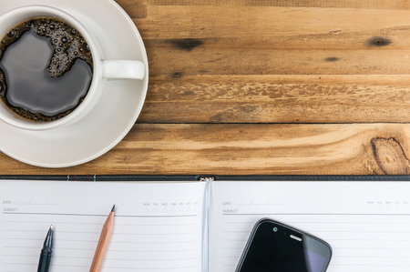notebook with pen, pencil, smart phone and coffee cup on wooden background の写真素材