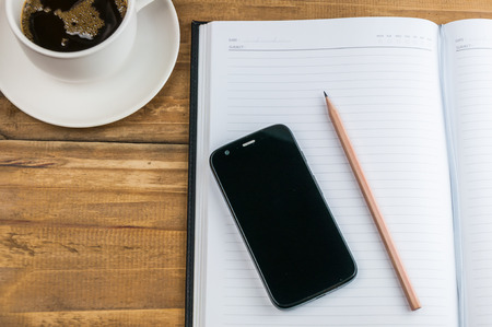 notebook with pencil, smart phone and coffee cup on wooden background 