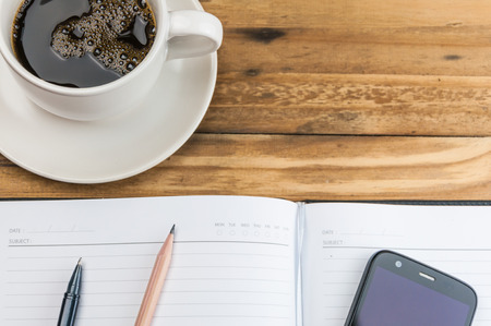 notebook with pen, pencil, smart phone and coffee cup on wooden background の写真素材