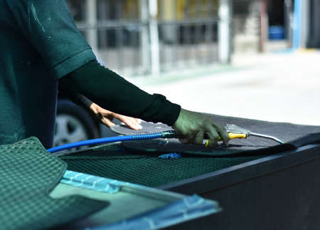 Car care shop. Worker holding blower head for cleaning dust on carpet. Cleaner clear and clean dirt...