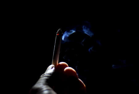 Silhouette smoky burn of cigarette in finger of people holding end of cigarette in dark night...