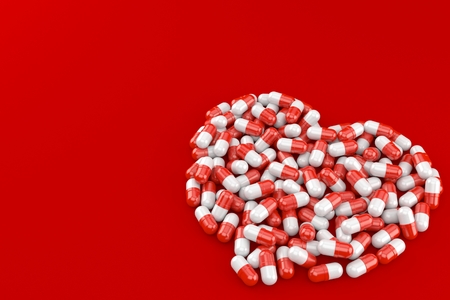 Heart symbol made from pills isolated on red backgroundの写真素材