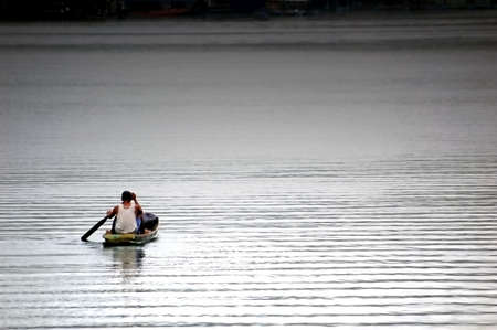 A lone Thai man paddling a boat across a lakeの写真素材