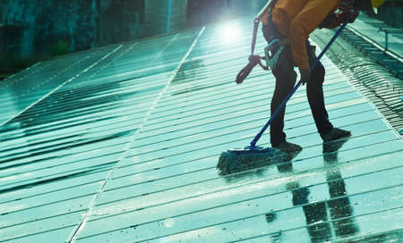 Photovoltaic technician is washing the surface of the panels on the roof of the building to increase efficiency of sun power to store and use the power inside the building below.の写真素材