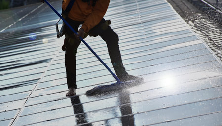 Photovoltaic technician is washing the surface of the panels on the roof of the building to increase...