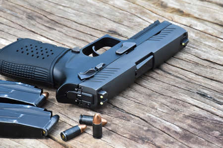 Automatic black 9mm pistol, ammunitions and cartridges on wooden table. Selective focus specific on...