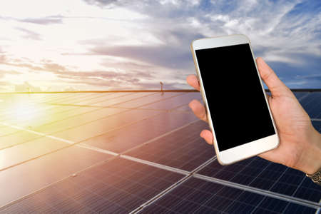 Mockup Mobile phone holding in hand with blurred solar roof background, concept for using smart devices with solar system at home, at work, on application and in daily life.の写真素材