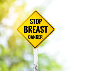 Yellow label traffic sign: âSTOP BREAST CANCERâ on cement pole beside the rural road with blurred background, campaign for drivers to support women's organizations working for breast cancer patients.の写真素材