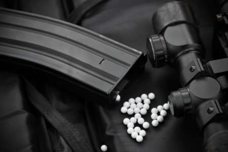 Closeup view of parts of airsoft gun with round white plastic bullets on a black leather background....