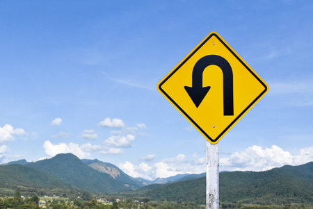 Traffic sign: Left U-turn sign on cement pole beside the rural road with white cloudy bluesky background, copy space.の写真素材
