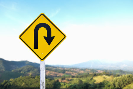 Traffic sign: Right U-turn sign on cement pole beside the rural road with white cloudy bluesky background, copy space.の写真素材
