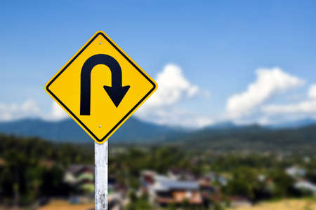 Traffic sign: Right U-turn sign on cement pole beside the rural road with white cloudy bluesky background, copy space.の写真素材