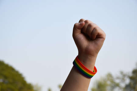 Asian young female in red t-shirt raises her left hand which has rubber rainbow wristband over her...