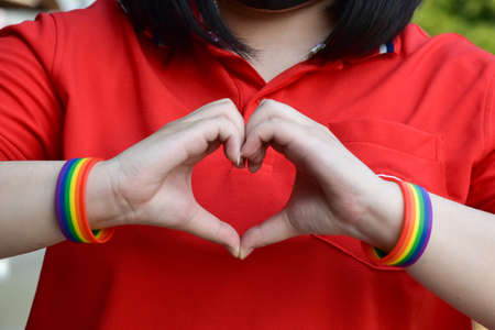 Asian young female makes heart shape by her fingers in the middle of her chest, soft and selective...