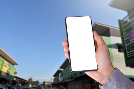 White blank touch screen smartphone holding in hand with blurr modern  buildings background. Close...