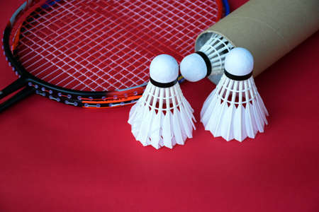 Cream white old and new badminton shuttlecocks and rackets on red floor in indoor badminton court,...