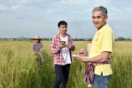 Asian senior volunteer wears yellow shirt and holds pen and notebook infront of asian young boy and...