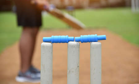 Closeup view of wickets, cricket sport equipments, blurred cricketer holding cricket bat on pitch background, concept for cricket sport lovers around the world.の写真素材