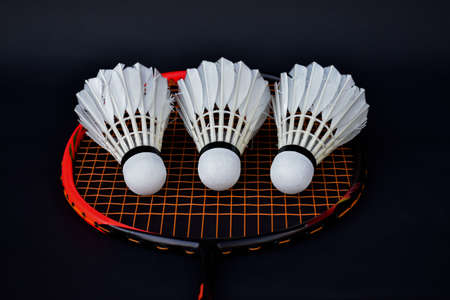 White cream badminton shuttlecock and badminton rackets on dark floor of indoor badminton court,...