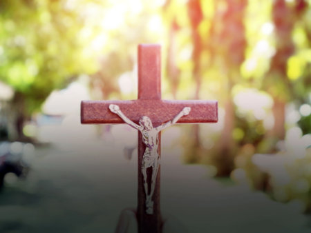 A black wooden cross with a statue of Jesus crucified by his arm. Behind it is the walk way of a school in an Asian country, soft and selective focus.の写真素材
